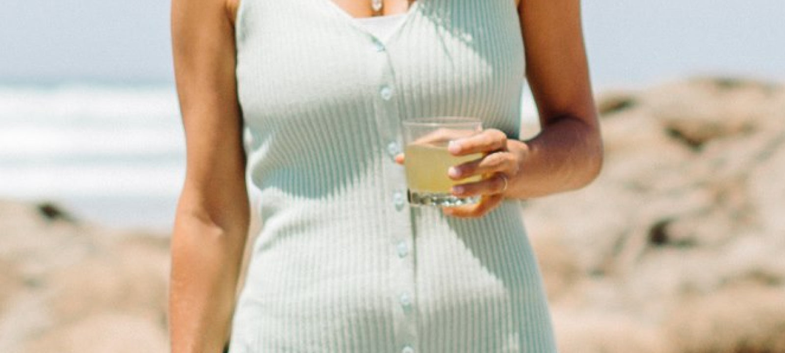 A woman in a teal top enjoying a Your Super drink at the beach